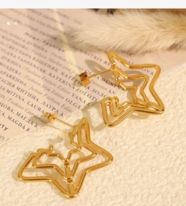 Detail of gold layered star earrings on a fashion magazine with soft yellow feathers