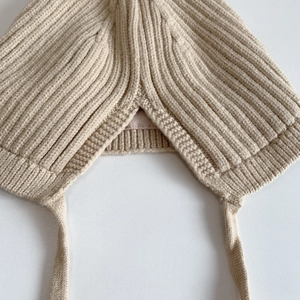 Detailansicht der beigen Baby-Strickmütze mit Ohrenklappen und feiner Textur der Bänder
