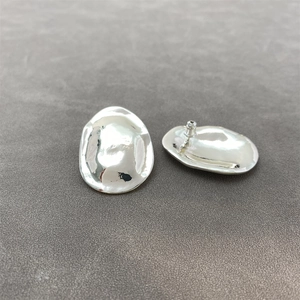 Close-up of silver irregular oval stud earrings featuring a molten lava texture