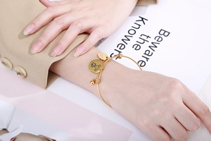 Detail of adjustable gold heart bracelet with girl tag charm on model wrist