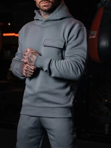 Close-up of grey fitness hoodie featuring a functional chest pocket in a gym setting