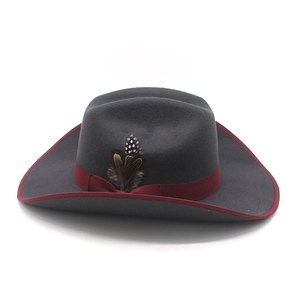 Detail of dark grey felt cowboy hat featuring a red ribbon band and a natural feather