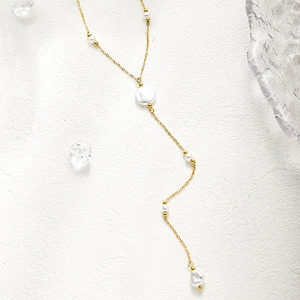 Detail of a gold plated Y-shaped necklace with white pearls and small beads
