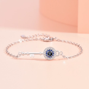 Elegant silver evil eye key bracelet with zircon inlay on a light pink background