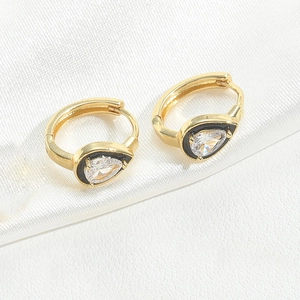 Detail view of gold teardrop hoop earrings with black enamel and clear stone on white silk