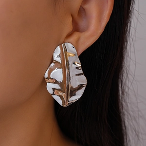Close-up of a silver irregular leaf earring with a crinkled metal texture on a model