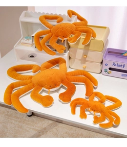 Three sizes of orange plush king crab toys arranged on a desk showing soft fur textures
