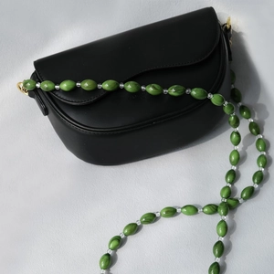 Detail of a black saddle bag featuring a unique green resin beaded chain shoulder strap