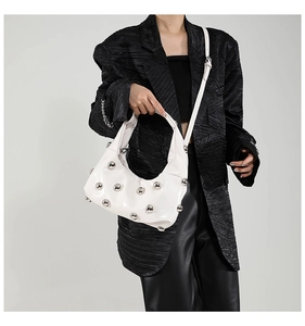 Detail shot of white glossy underarm bag featuring silver round metal rivets on a leather strap