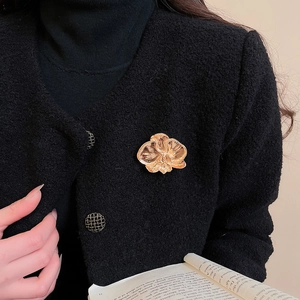 Detailed close-up of a golden orchid flower brooch pinned on a black tweed blazer coat