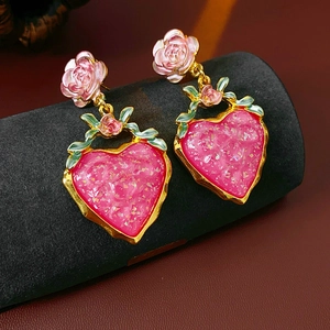 Detailed close-up of pink rose heart earrings with gold trim on a velvet stand