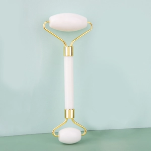Close-up of dual-head white jade roller with gold metal brackets for facial massage