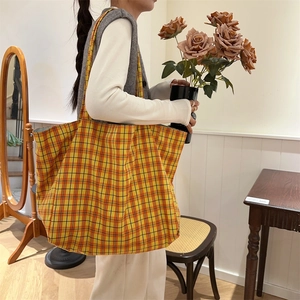 Detail of a large orange checkered canvas tote bag worn by a model in a warm room