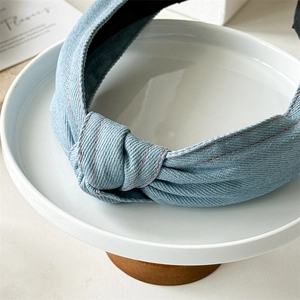 Détail d'un serre-tête en denim bleu clair avec coutures roses et nœud sur support blanc