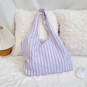 Detailed view of blue and pink striped canvas tote bag on white bed with lifestyle decor