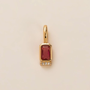 Macro shot of gold pendant with rectangular red gemstone and diamond accents