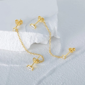 Close-up of gold chain earrings with clear gemstones on textured white stone background