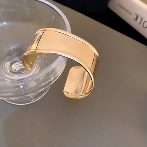 Close-up of wide polished gold bangle with irregular folds on a glass container
