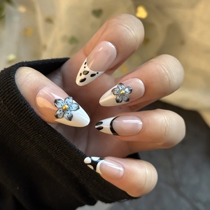 Gros plan de fleurs 3D bleues sur faux ongles amande de style français avec taches noires