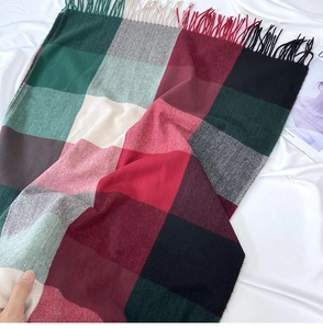 Detail of red and green plaid scarf with long fringe tassels on white fabric