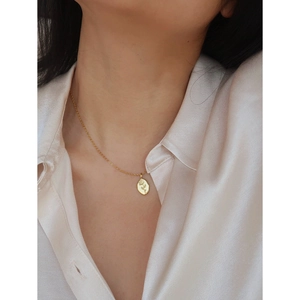 Close-up of golden rose oval pendant necklace on a silk shirt for elegant jewelry styling