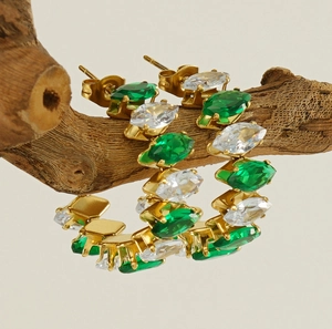 Dettaglio di orecchini a cerchio dorati con zirconi verdi su un ramo di legno