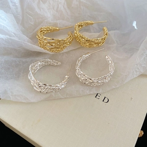 Detail of gold and silver twisted C-shape earrings with textured woven metal design