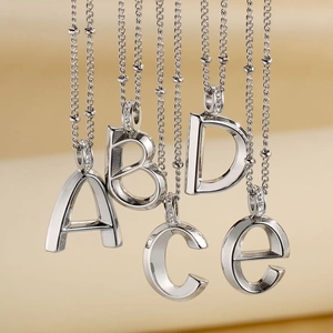 Detailed view of silver crystal-inlaid A, B, C, D, E letter charms on titanium necklaces