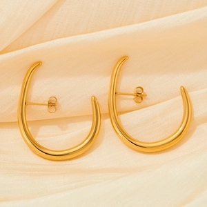 Macro shot of gold U-shaped geometric earrings on elegant champagne silk fabric