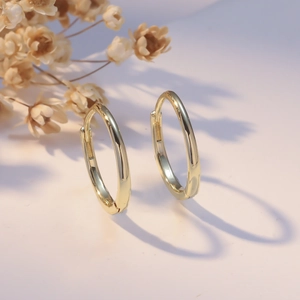 Polished gold hoop earrings with cylindrical design on minimalist neutral background