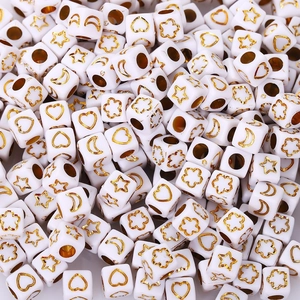 Macro shot of white acrylic cube beads with gold star heart and moon patterns for DIY jewelry