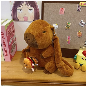 Plush brown capybara backpack bag with a small hamburger charm on a warm wooden desk
