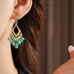 Detailed close-up of Bohemian gold teardrop earrings with green beads and white pearls