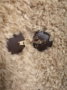 Macro detail of polished metal buckle on fleece jacket with brown leather trim
