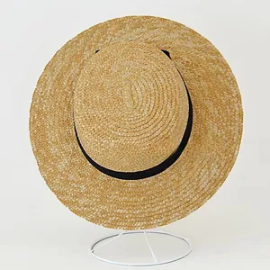 Detail of natural straw boater hat featuring a flat top and black ribbon decoration