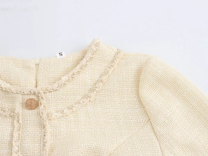 Macro detail of beige tweed dress neckline with woven trim and decorative gold button