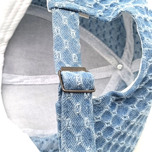 Detail of adjustable bronze metal buckle on light blue washed denim baseball cap