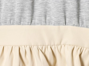 Detailaufnahme von grauem Strickstoff mit angenähten beigen Falten-Rüschendetails