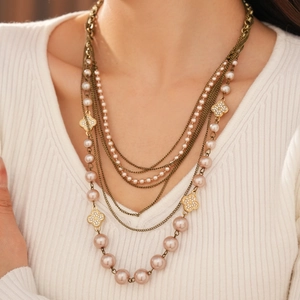 Detail shot of multi-layer pearl necklace featuring diamond-set clover charms on knits