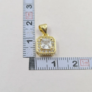Detailed view of square gold pendant with zircon stone and ruler measuring size
