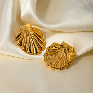 Detail of 18k gold scallop shell earrings resting on beige silk fabric texture