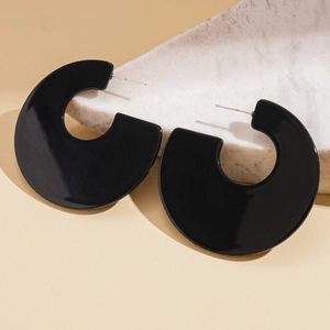 Detailed view of large black acrylic C-shaped earrings on a textured stone prop