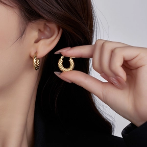 Close-up of golden textured round hoop earrings in titanium steel worn by a model