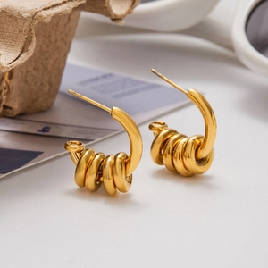 Macro shot of gold C-shaped earrings with layered stack rings on a fashion magazine