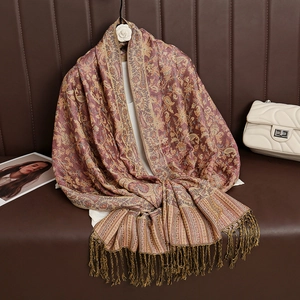 Detail of luxury paisley jacquard scarf with tassels on a leather sofa with a white bag