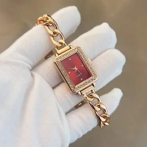 Close-up of golden rectangular watch with red dial and rhinestone bezel on a chain strap