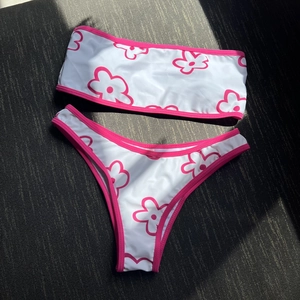 Detailed flat lay of floral bandeau bikini set with pink trim on textured background