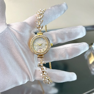Detail showing leaf-shaped watchband with diamonds and pearl dial on a gold quartz watch