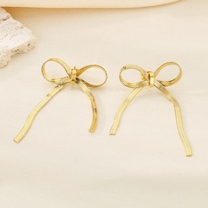 Close-up of golden bow earrings featuring elegant snake chain ribbon details on stone