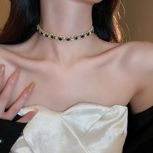 Gros plan d'un choker doré avec une pierre carrée verte et des diamants pavés blancs